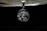 A silver pendant depicting a religious figure with a crown of thorns is hanging against a dark background. Above it, the edge of an old book with visible pages can be seen, casting a shadow.