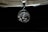 A silver pendant depicting a religious figure with a crown of thorns is hanging against a dark background. Above it, the edge of an old book with visible pages can be seen, casting a shadow.