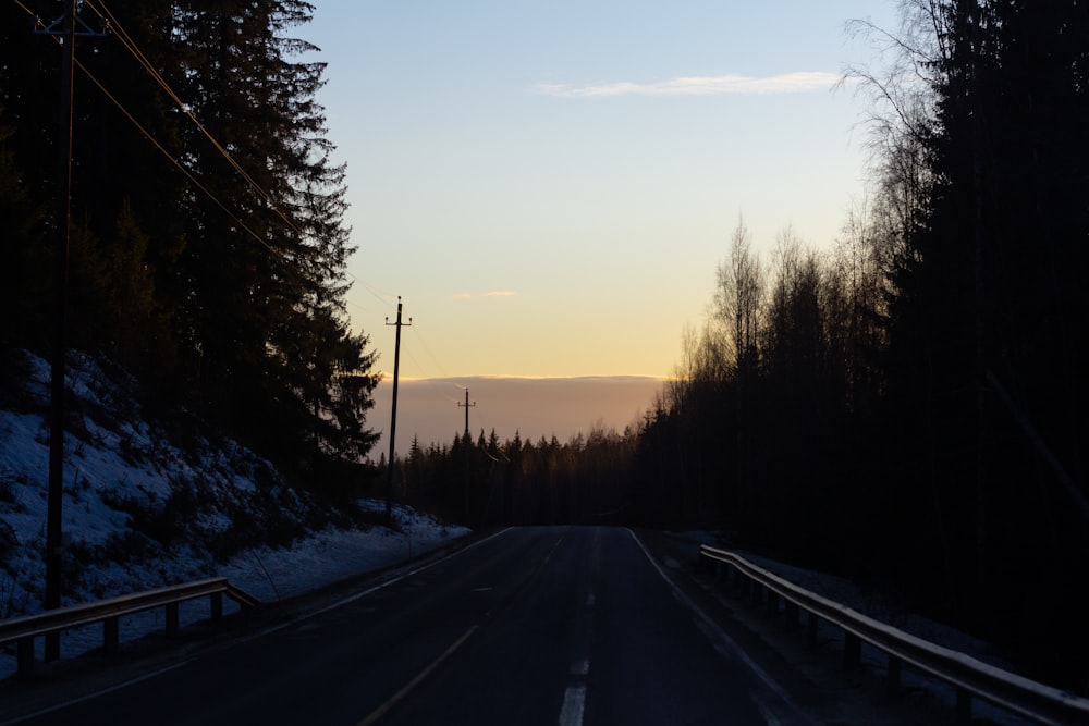 black asphalt road between snow covered ground during sunset