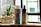 A bottle of CBD Pain Freeze spray and a dropper bottle of CBD Vanilla oil are placed on a wooden surface. Next to them is a small glass planter with a succulent, filled with pebbles and sand. The background features a softly blurred window, suggesting natural light entering the room.