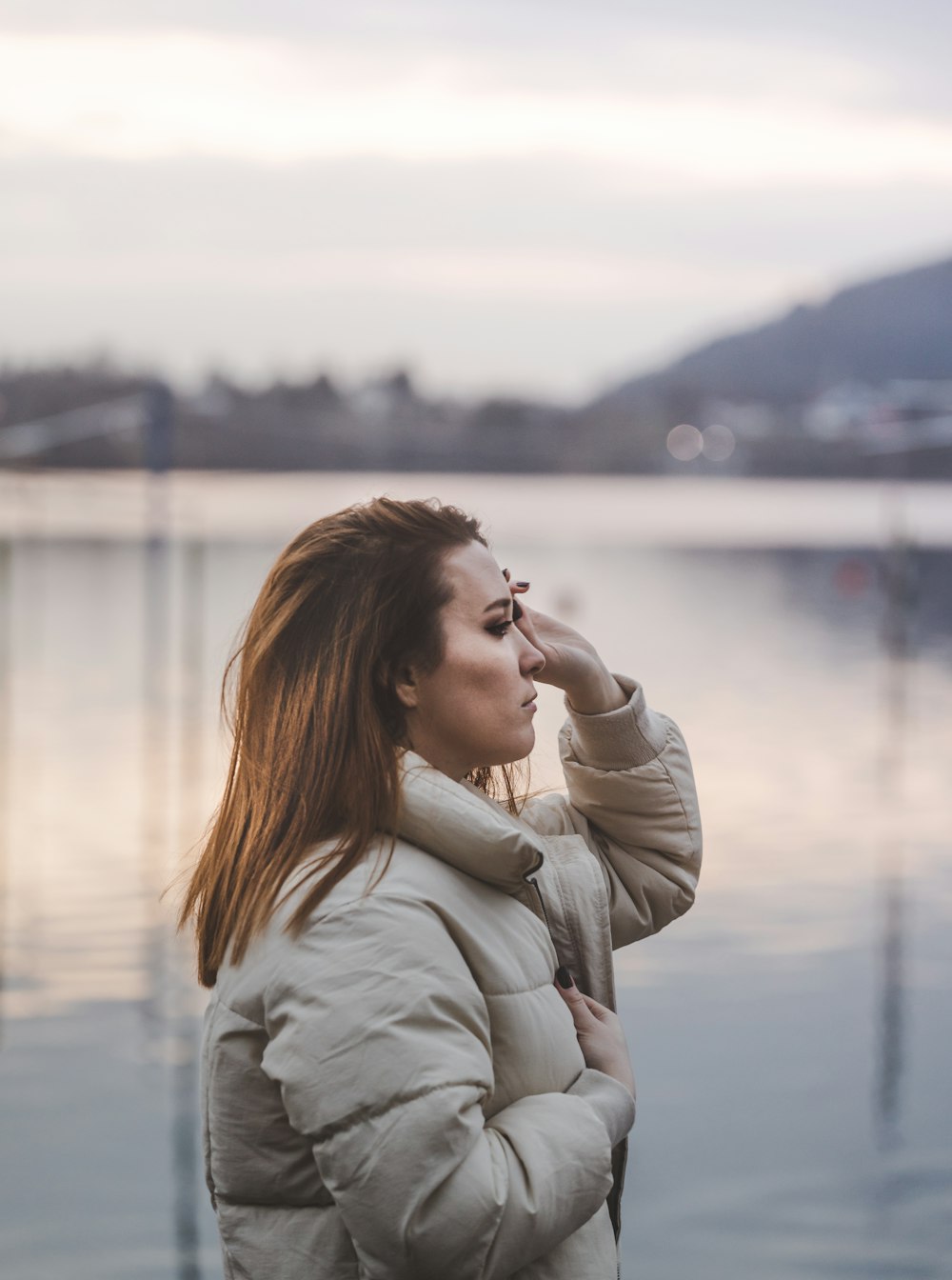 woman in gray coat standing near body of water during daytime