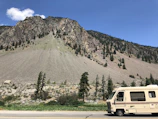 A cozy RV parked beside tall pine trees under a clear blue sky.