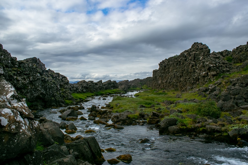 green and brown rocky mountain beside river under blue and white cloudy sky during daytime