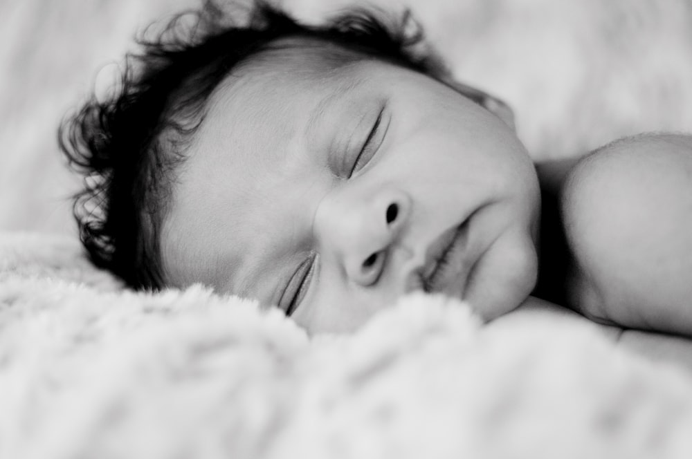 grayscale photo of baby lying on white textile