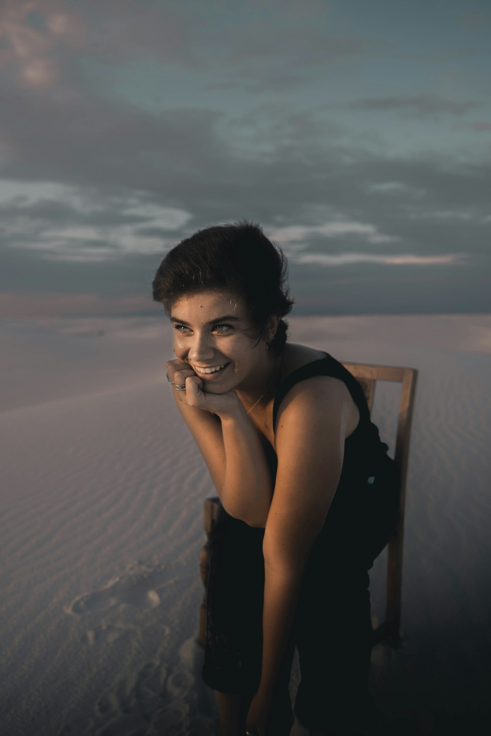 woman in black tank top sitting on brown wooden chair on brown sand during daytime