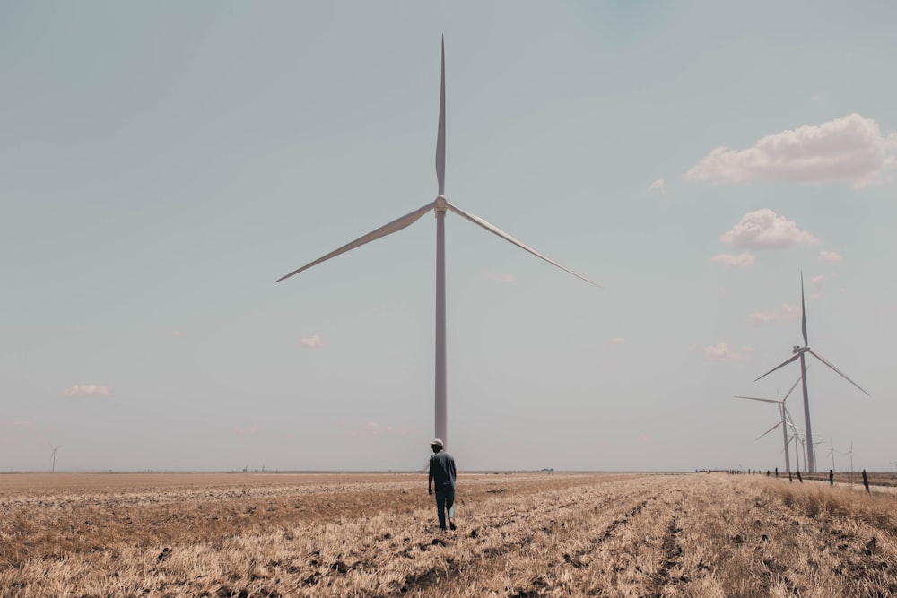 person in black jacket walking on brown sand near white wind mill during daytime