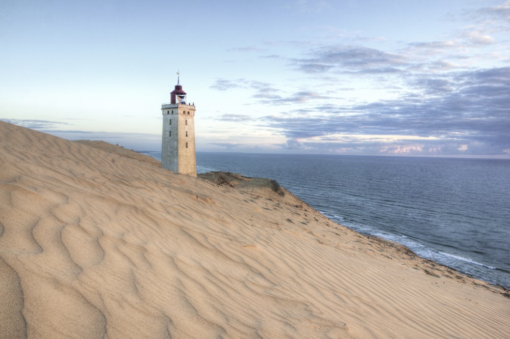 white and brown concrete lighthouse on brown sand near body of water during daytime