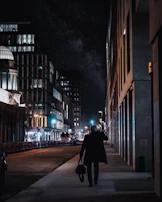 A lone figure walking along a city roadside under a starry night sky, deep in thought.