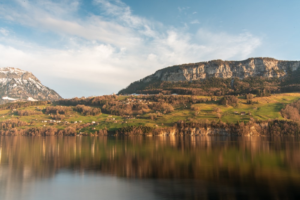 green and brown mountain beside body of water under blue sky during daytime