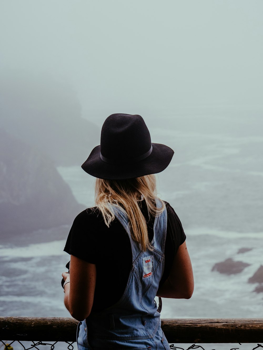 Donna in cappello nero e maglietta blu in piedi in riva al mare durante il giorno