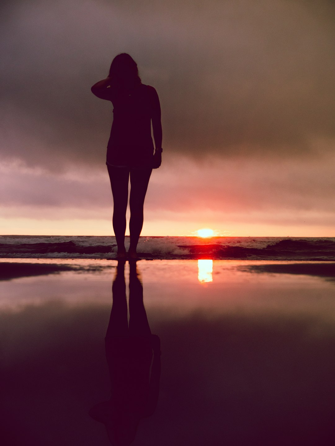silhouette of woman standing on seashore during sunset