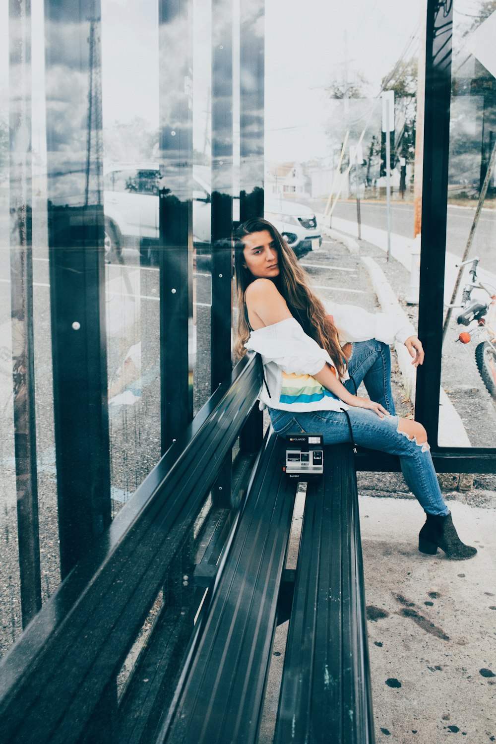 woman in white shirt and blue denim jeans sitting on brown wooden bench