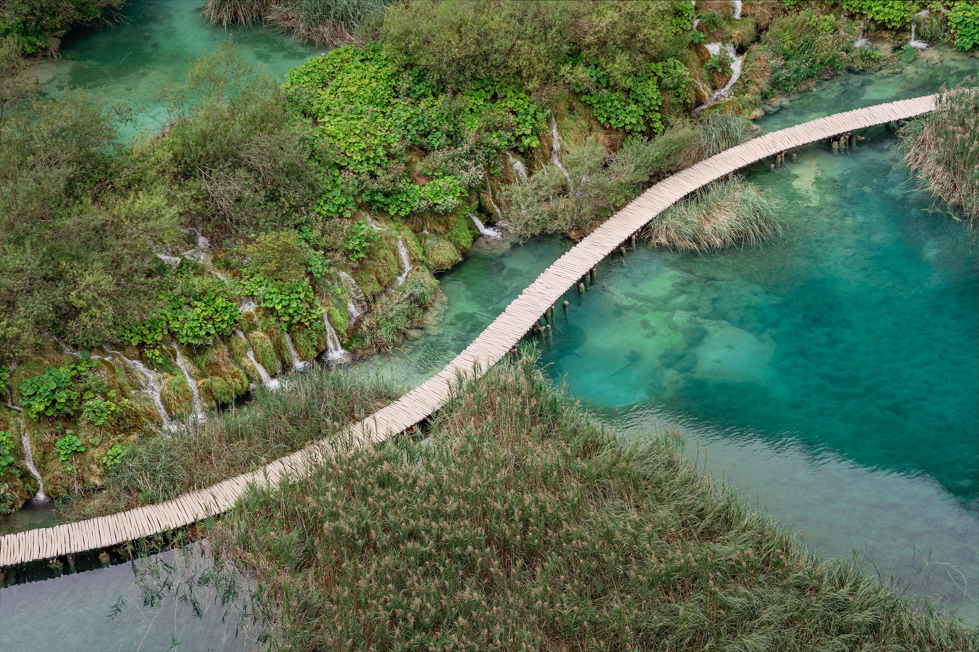 A wooden boardwalk over the turquoise pools and small cascades of the Plitvice Lakes