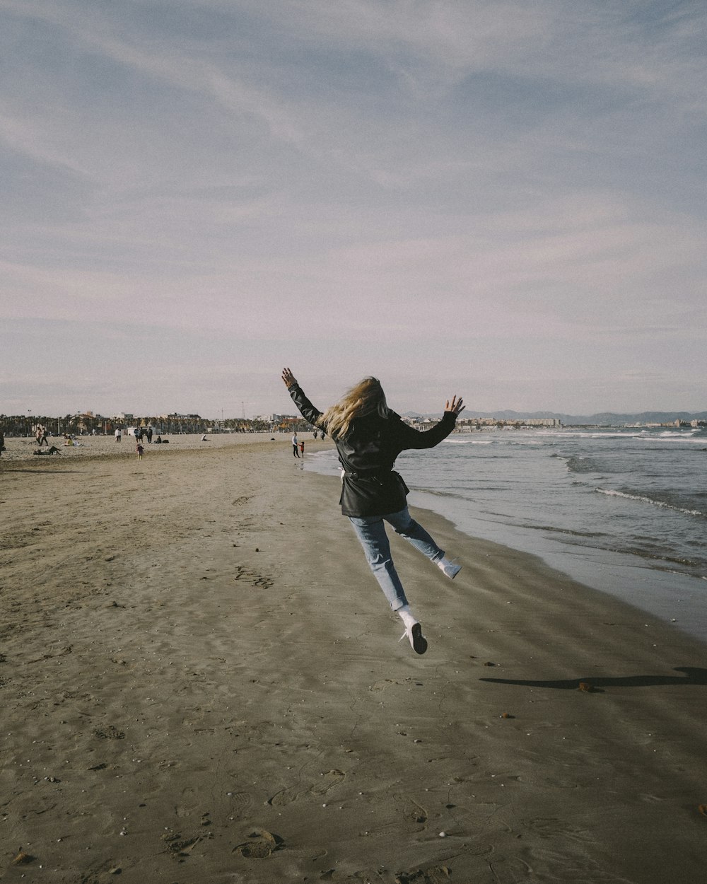 man in black jacket and blue denim jeans jumping on beach during daytime