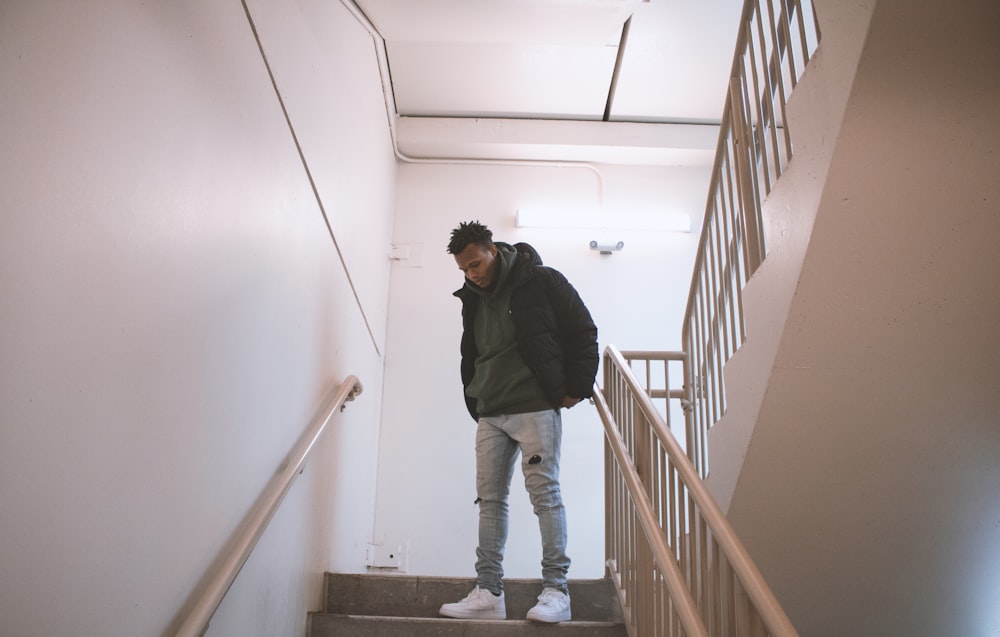 man in black jacket and blue denim jeans standing on stairs