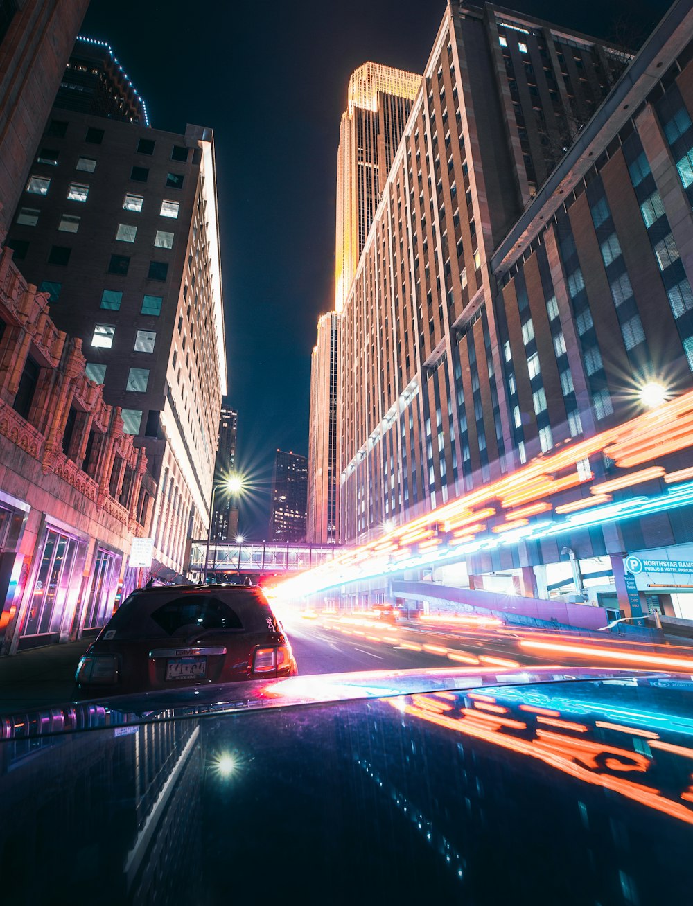 red car on road in between high rise buildings during night time