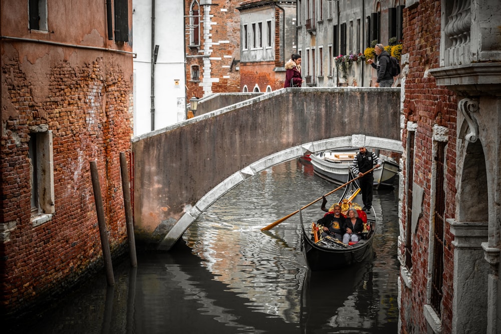 man in black boat on river between concrete buildings during daytime