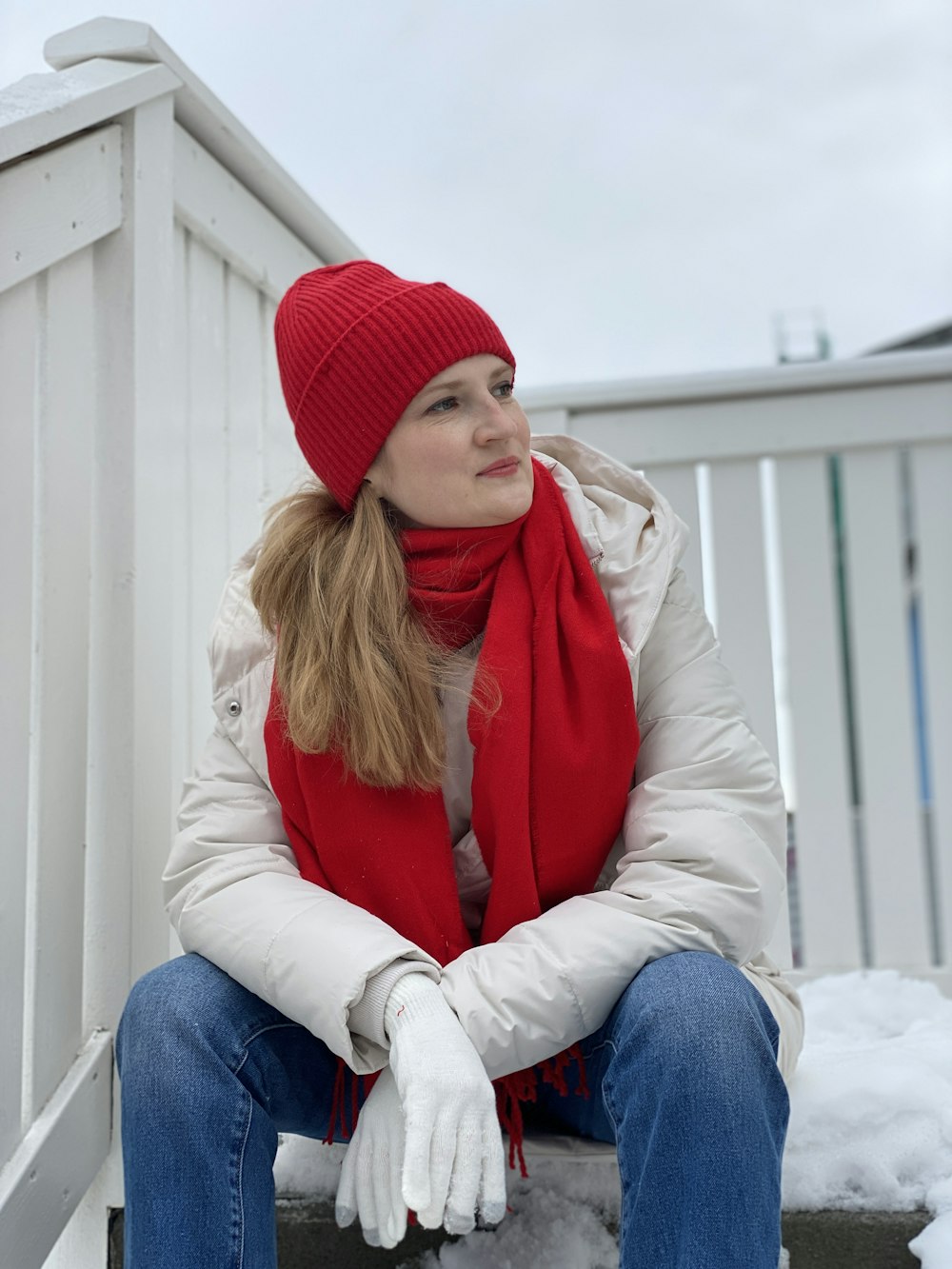 woman in red knit cap and white jacket sitting on white wooden bench during daytime