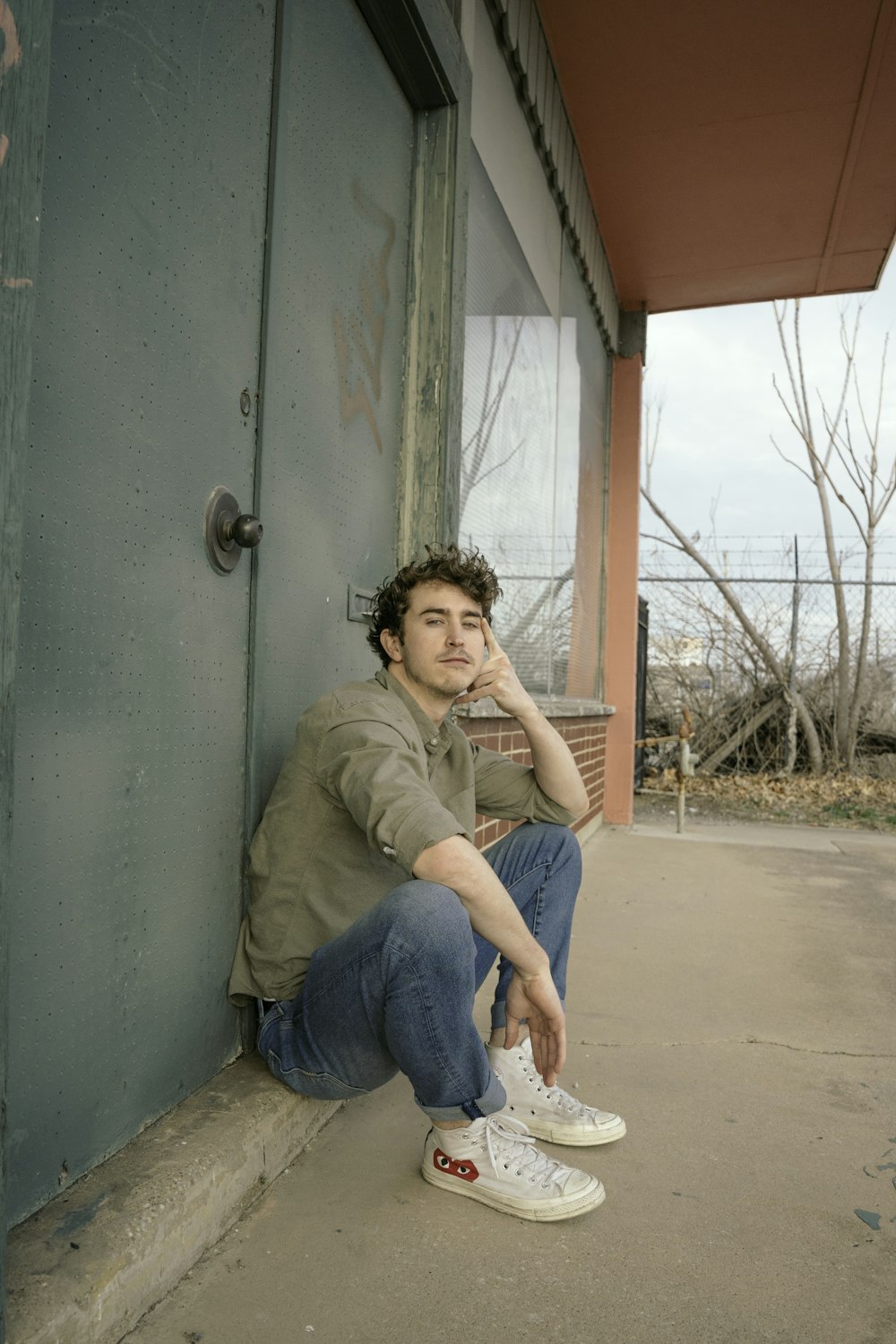 woman in brown jacket and blue denim jeans sitting on concrete bench