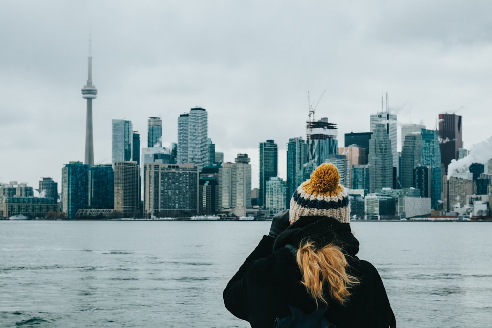 woman in black and brown parka jacket standing near body of water during daytime