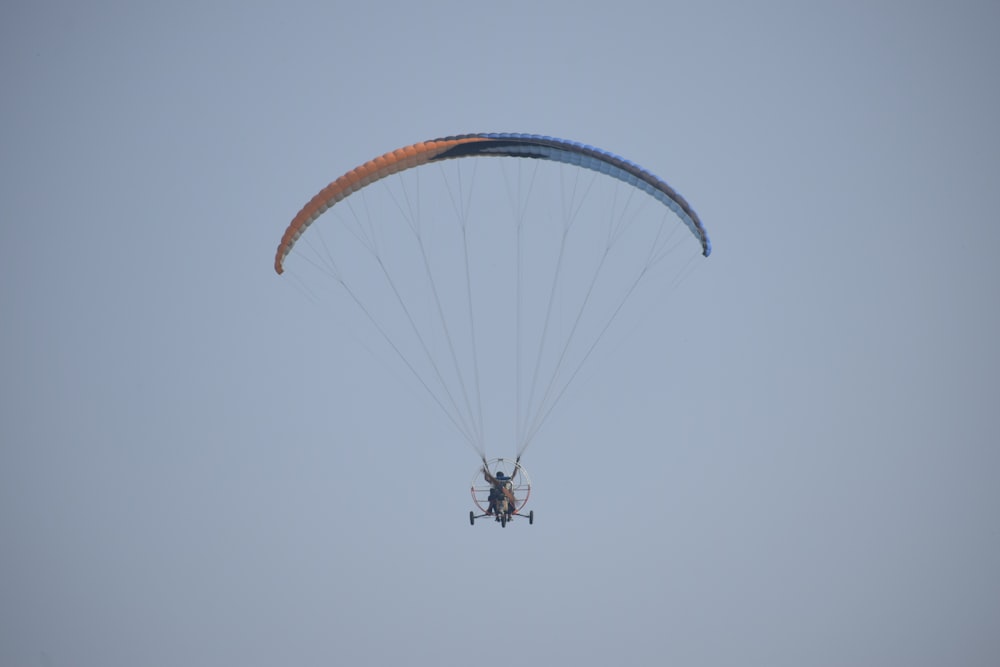 person in black jacket and blue jeans riding on orange parachute