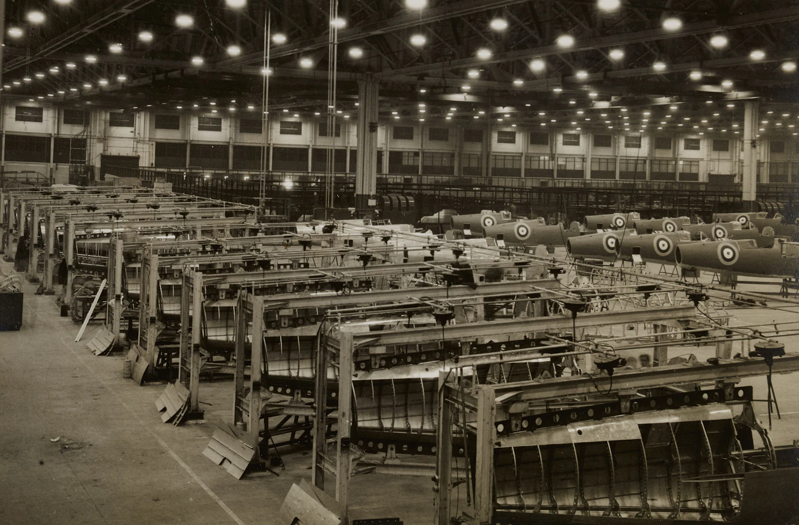 Grayscale interior of a wartime aircraft factory, rows of machines stretching into the distance