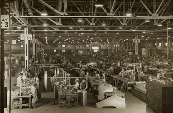 Photo of a factory floor with workers operating machinery and safety signs visible.