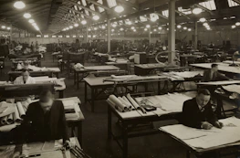 An outside view of a furniture factory with workers collaborating on designs.