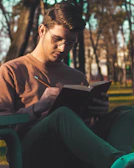 man in brown long sleeve shirt sitting on green plastic chair reading book