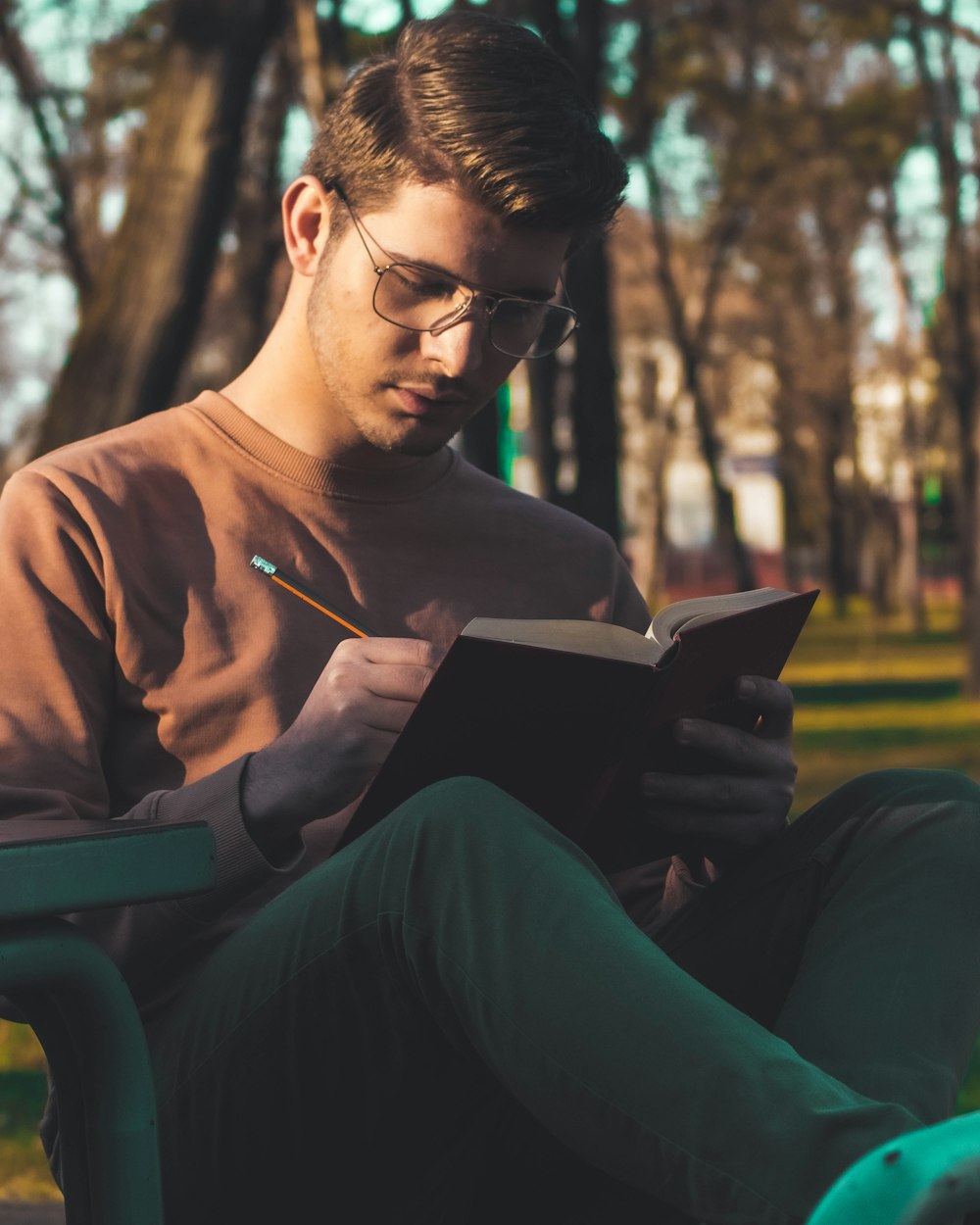 갈색 긴 소매 셔츠를 입은 남자가 녹색 플라스틱 의자에 앉아 책을 읽고 있다