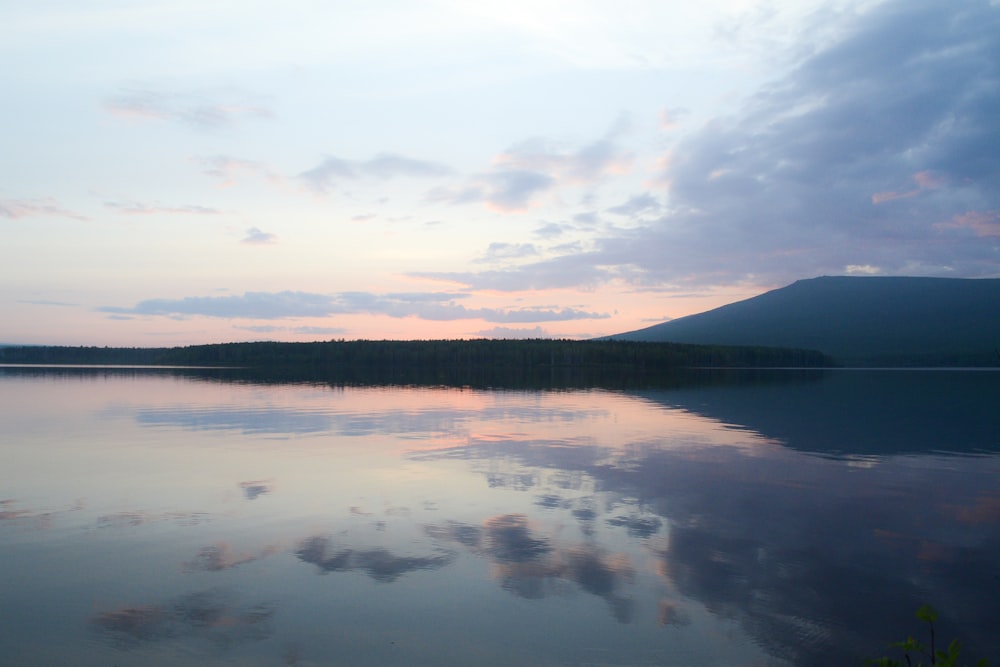 body of water near green trees under white clouds during daytime