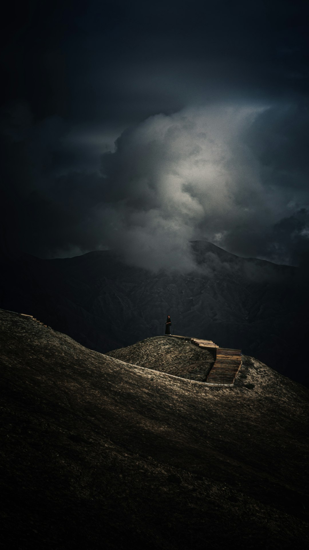 person standing on rock near mountain under cloudy sky during daytime