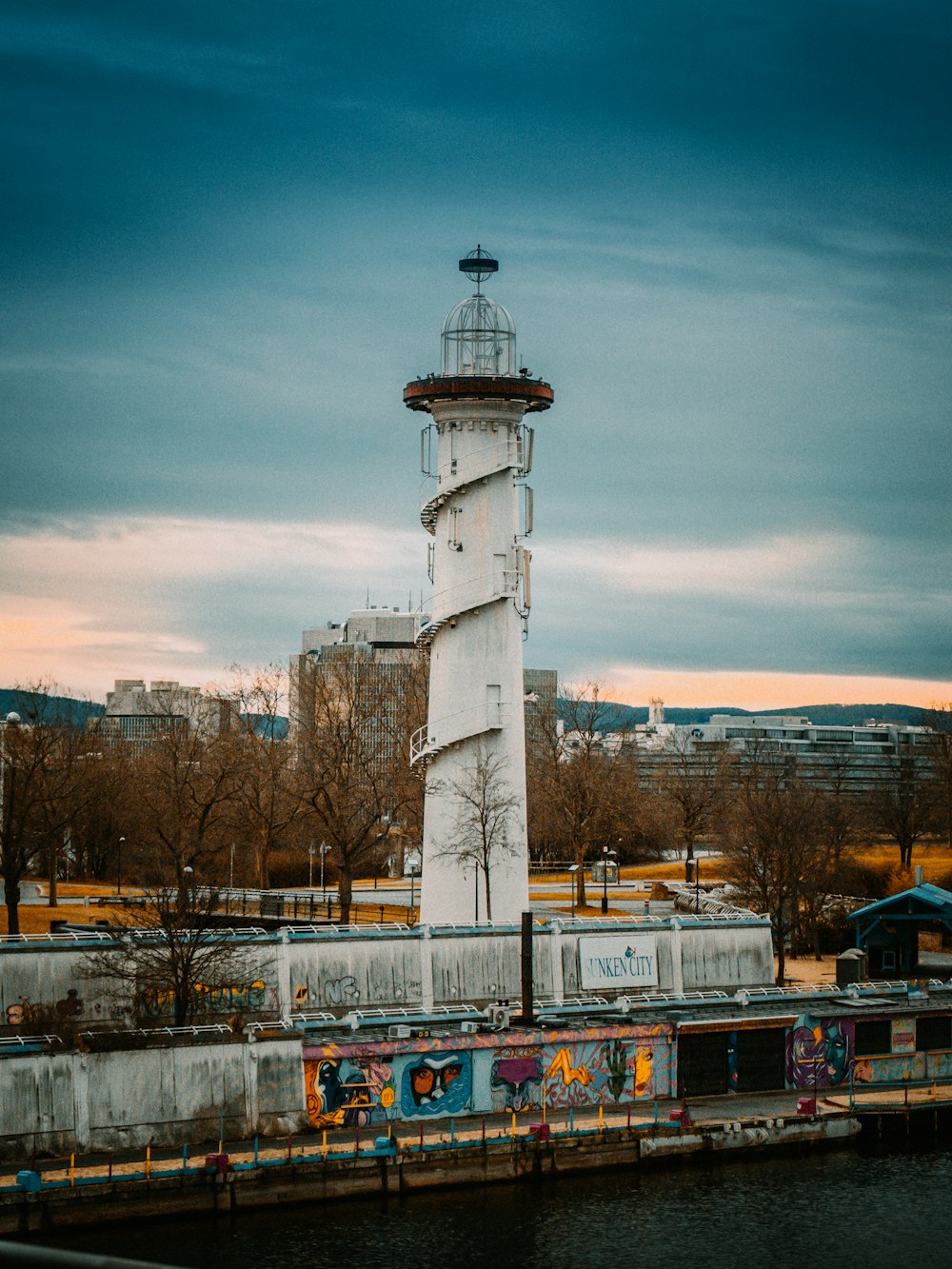 white and black lighthouse near bare trees under blue sky during daytime