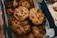 A box of freshly baked chocolate chip cookies is arranged neatly, with visible chocolate chunks scattered throughout the golden brown surface of each cookie.