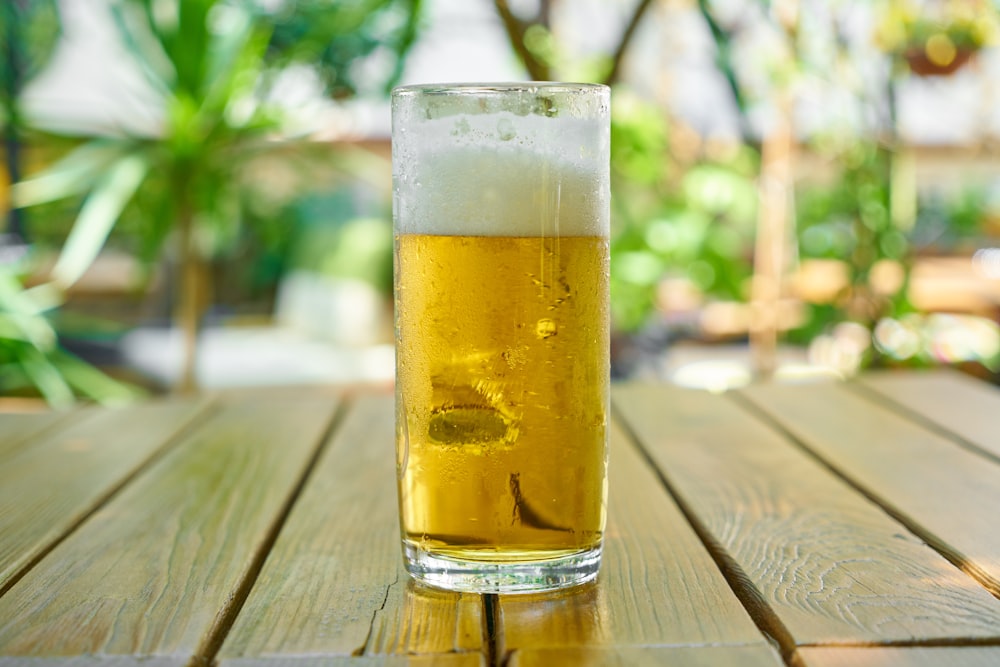 Vaso transparente con cerveza sobre mesa de madera marrón