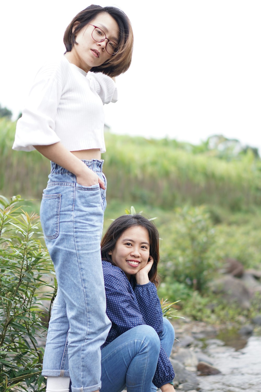 girl in white t-shirt and blue denim jeans standing on green grass field during daytime