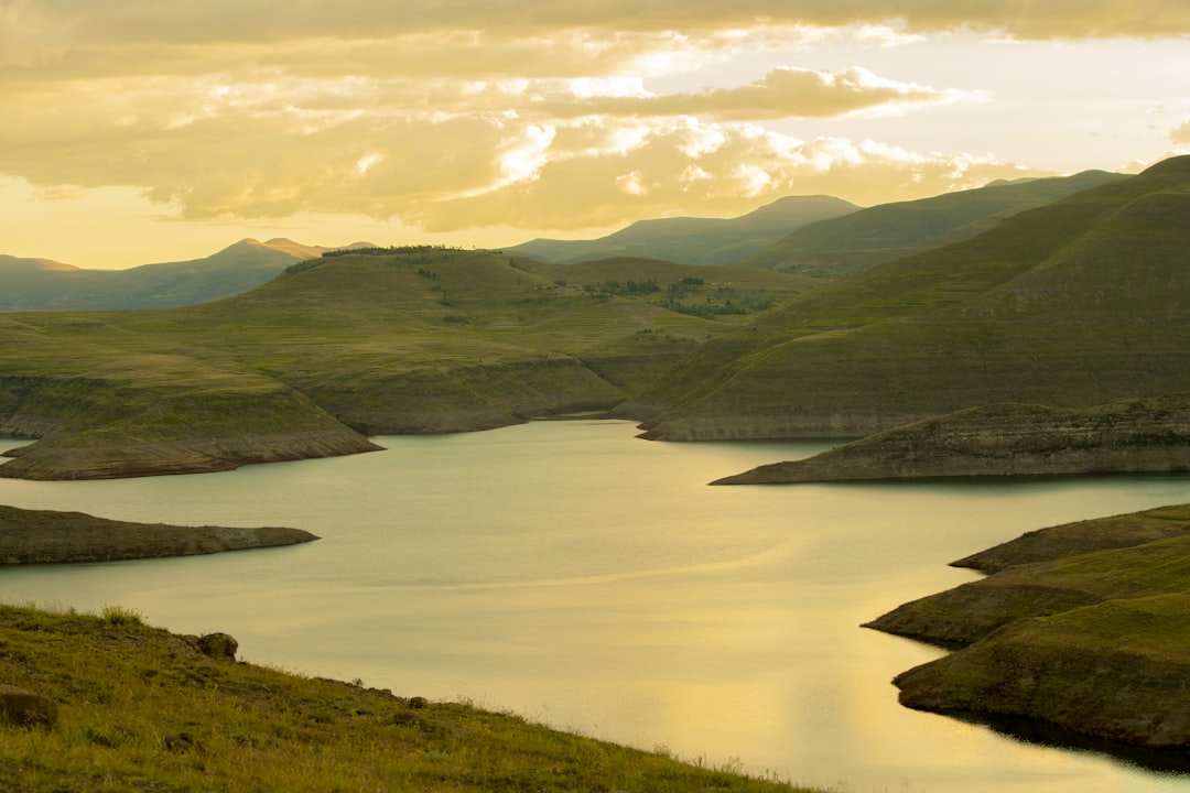 green mountains near body of water under white clouds during daytime