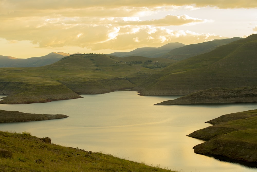 green mountains near body of water under white clouds during daytime