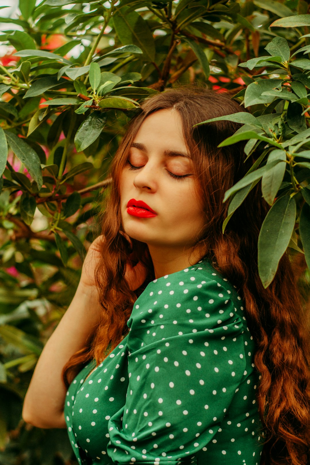 woman in green and white polka dot sleeveless dress standing beside green leaves