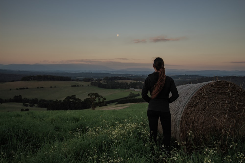 woman in black jacket standing on green grass field during sunset