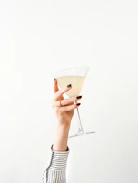 Close-up of elegant hands holding a sparkling cocktail glass in a dimly lit lounge.