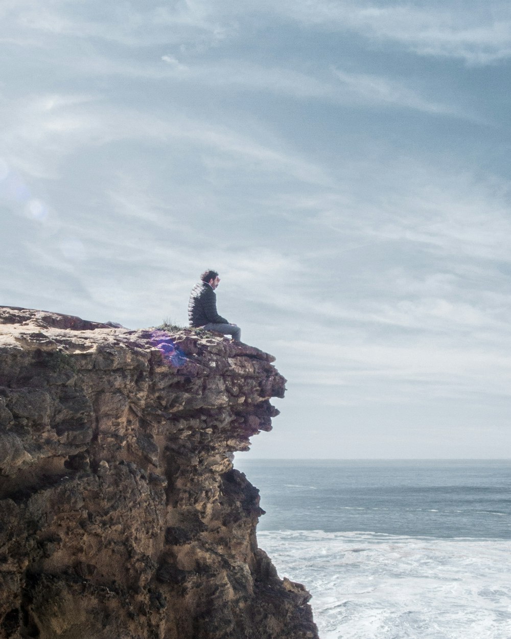 man in blue shirt sitting on brown rock formation during daytime