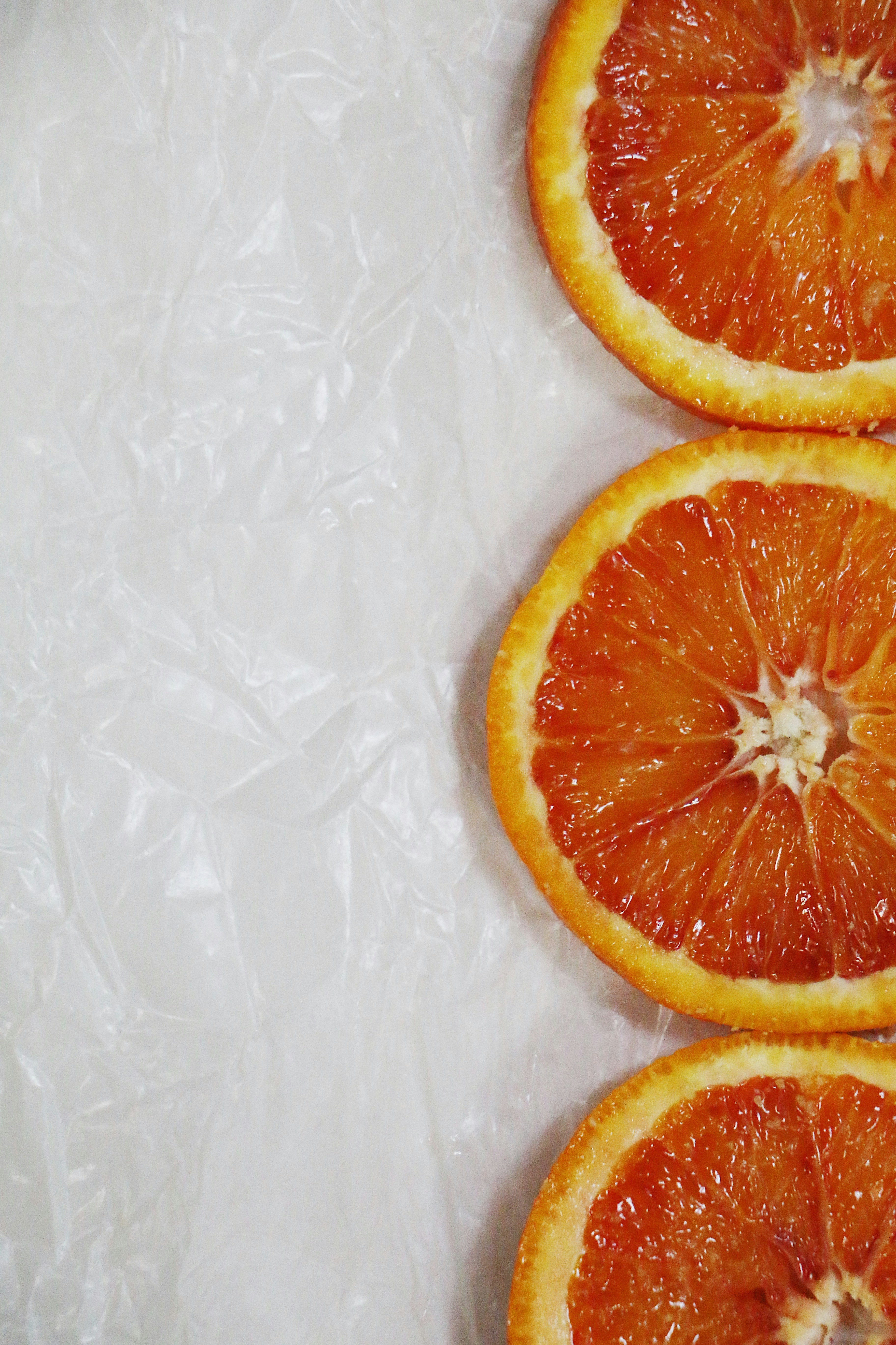 Fresh orange slices and whole oranges on warm cream background, bright natural sunlight, vibrant citrus colors