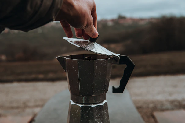 Hands using a moka pot on a stove, showing the brewing process of fresh coffee.