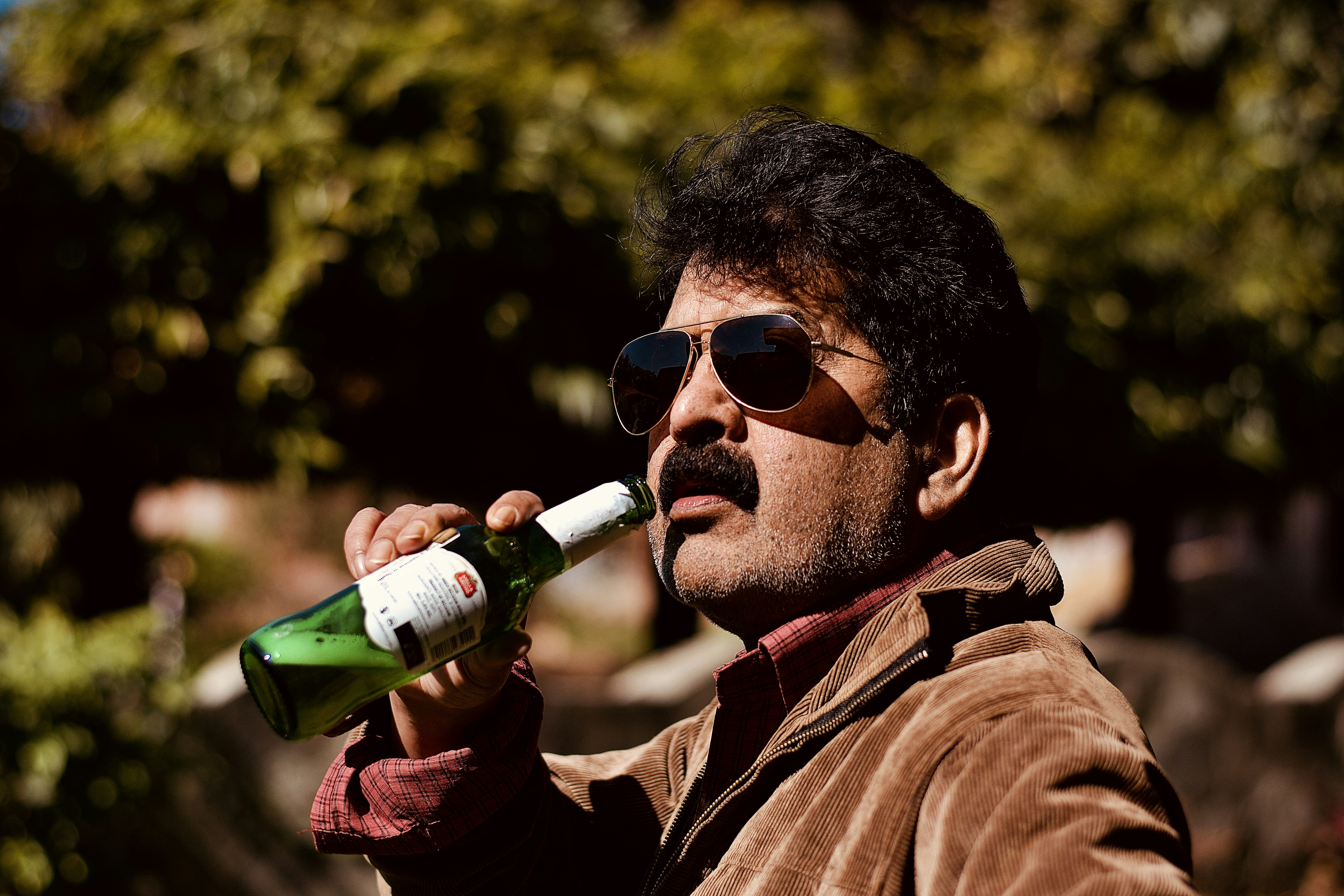 man in brown jacket holding green glass bottle