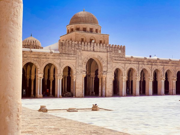 حیاط مسجد جامع قیروان با رواق‌های ستون‌دار و گنبدهای شیاردار زیر آسمان آبی