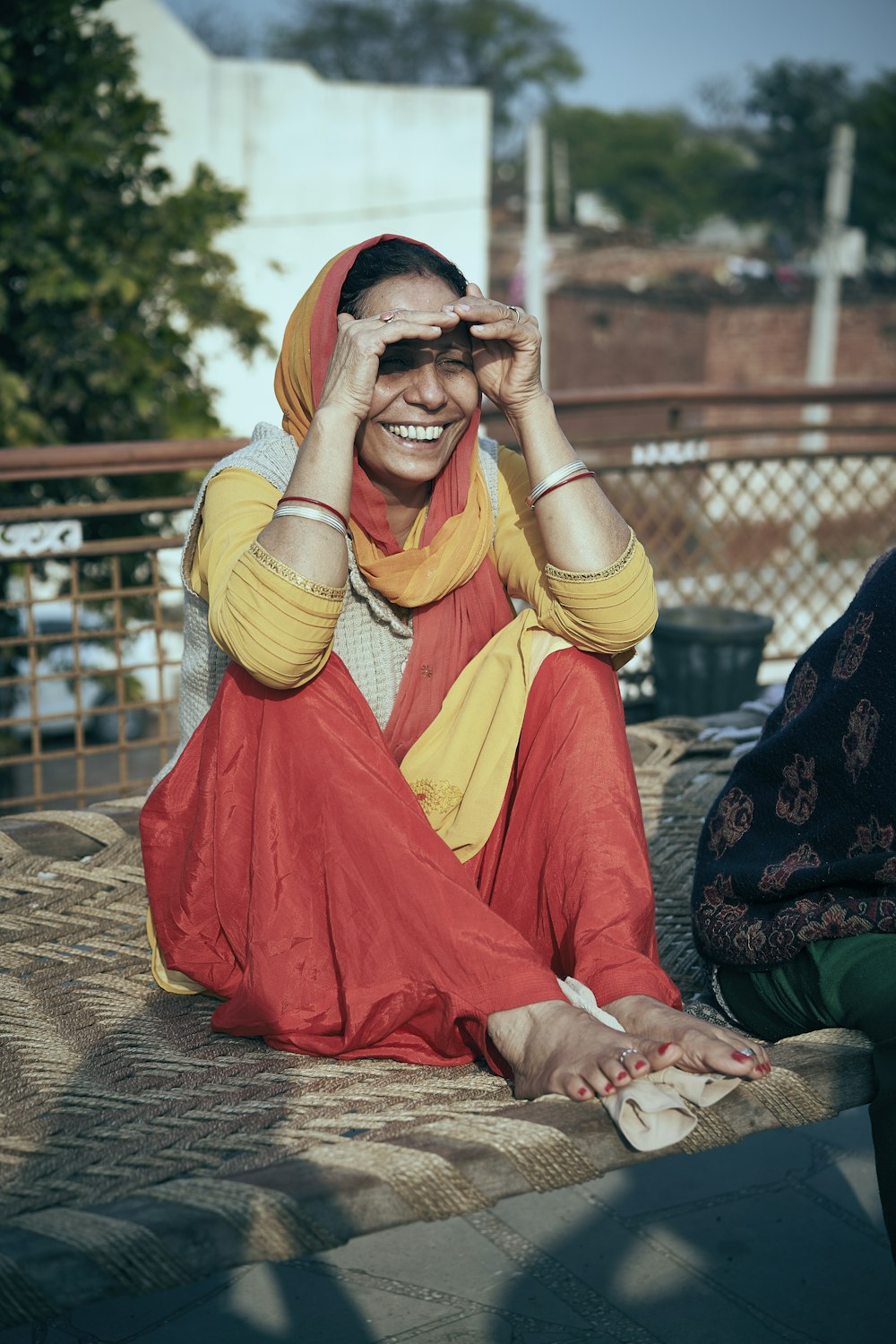 Mujer en sari amarillo y rojo sentada en el suelo de hormigón marrón