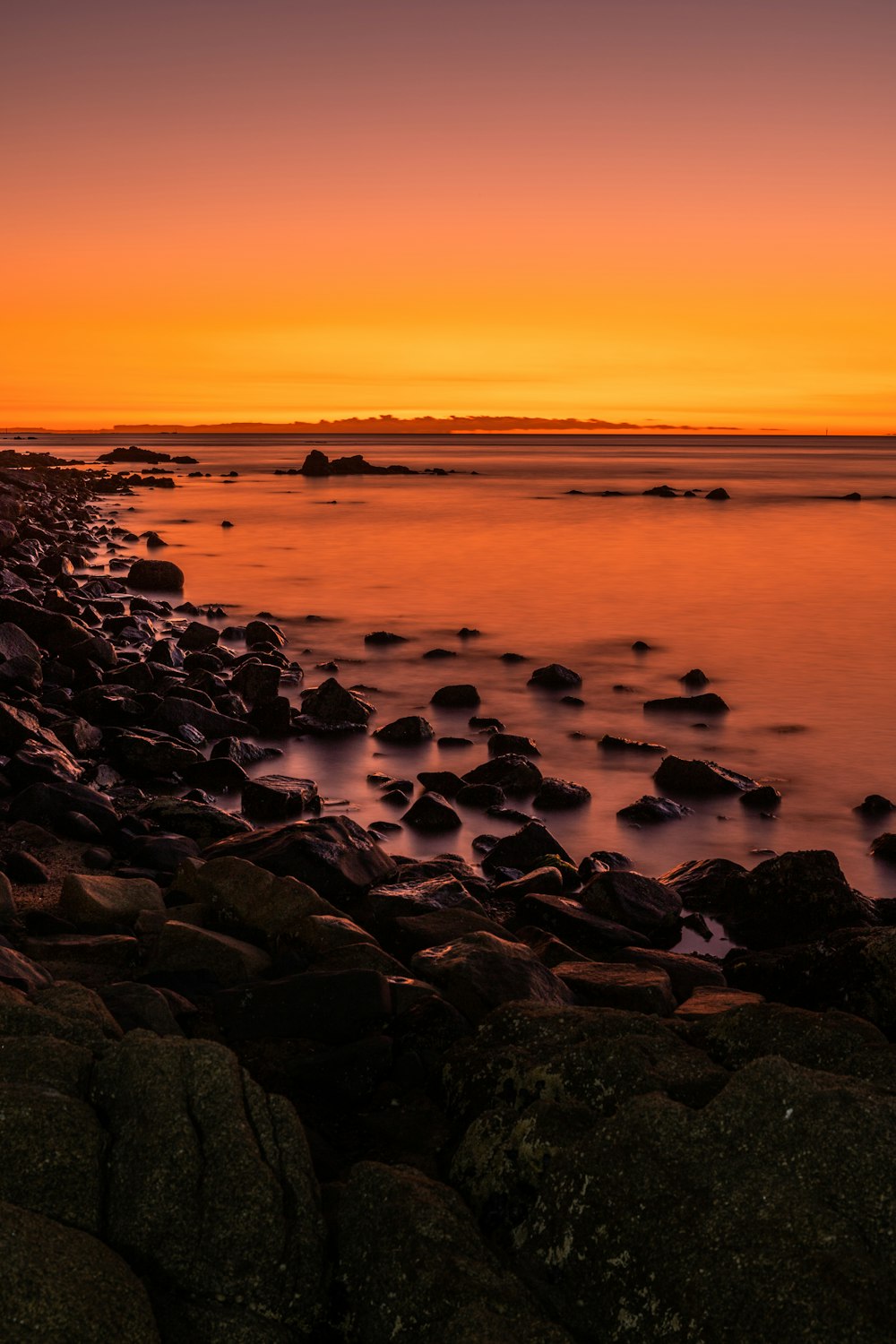 black and brown rocks on seashore during sunset