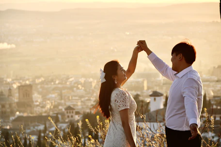 A couple dressed in elegant ceremonial attire standing on a sunlit rooftop with NYC skyline behind.