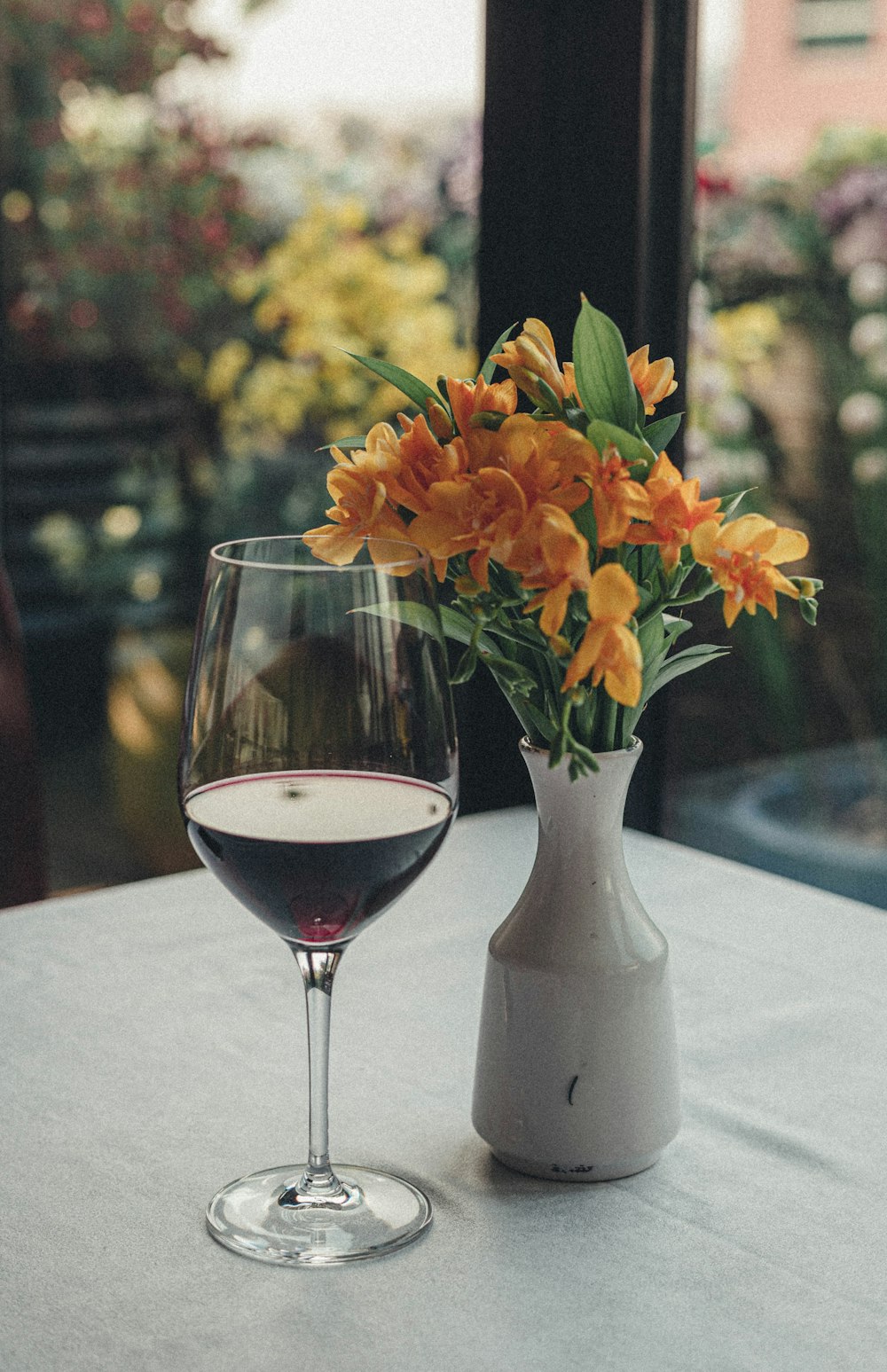 orange flowers in white ceramic vase beside clear wine glass